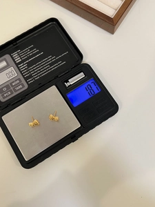 Detail shot showing the 1.87g weight of gold bow earrings on a digital scale