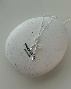 Dettaglio collana con pendente a fiocco in argento e cristalli su flacone di profumo
