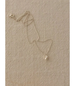 Détail du collier noeud en argent 925 avec perle blanche sur fond en lin beige