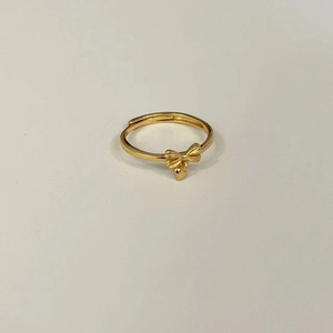 Close-up of golden bow ring with heart pendant and adjustable open band on grey background