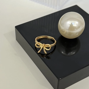 Macro shot of an adjustable 18K gold bow ring on a black display stand with a pearl