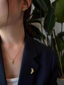 Détail du collier et de la broche croissant dorés avec une texture plissée élégante