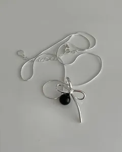 Detail of S925 silver bow necklace with black pearl pendant and sleek snake chain link