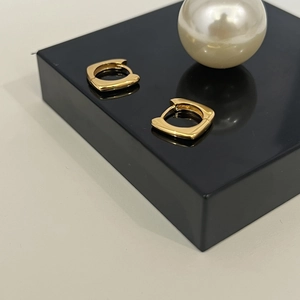 Gros plan de boucles d'oreilles carrées plaquées or 18K sur support noir avec perle