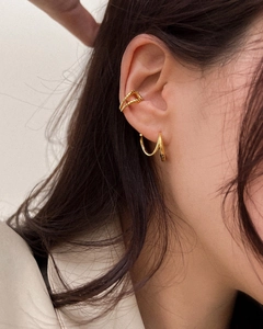 Close-up of golden geometric twist ear cuff and spiral stud earrings on a model