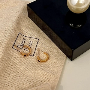 Gold C-shaped earrings with vintage engraving and black zircon on a beige linen pouch