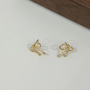 Close-up of golden metal bow earrings with a textured ribbon design and minimalist style
