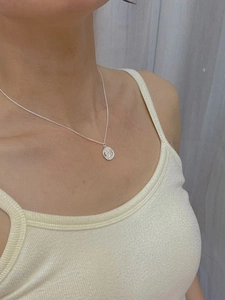 Close-up of silver coin pendant necklace with portrait relief on a minimalist chain