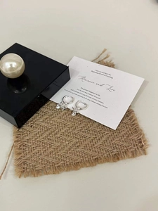 Detailed view of silver bow earrings with zircon pendant on a textured woven mat
