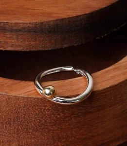 Vue macro d'une bague minimaliste en argent 925 avec perle dorée sur bois sombre