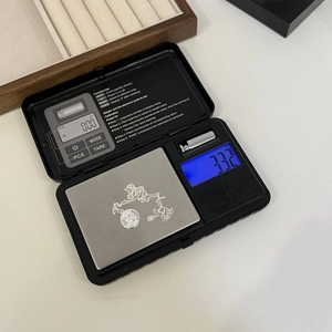 Macro view of a digital pocket scale weighing a silver coin necklace on a metal plate