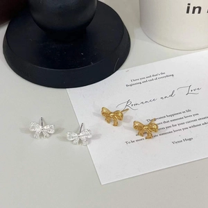 Detailed view of silver and gold hollow bow stud earrings on a poetic card