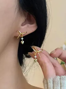 Close-up of gold bow earrings with clear zircon and heart pendants for women