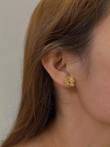 Close-up of elegant gold bow earrings with sparkling pavé stones worn by a model