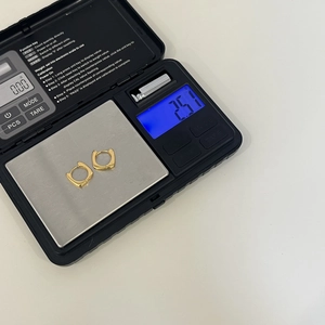Détail de boucles d'oreilles carrées dorées pesant 2,51g sur une balance numérique