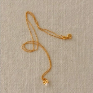 Collier en argent 925 doré avec pendentif nœud et perle sur un tissu en lin naturel