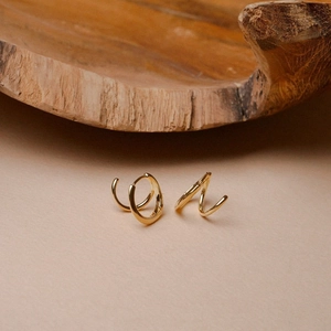 Elegant gold geometric spiral twist earrings displayed on minimalist wooden props
