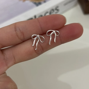 Detailed close-up of delicate silver bow earrings in a stylish ribbon design held by hand