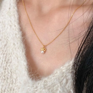 Élégant collier en argent 925 avec pendentif nœud et perle sur un pull blanc doux