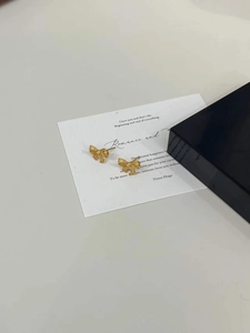 Detailed view of gold-plated hollow bow earrings with woven texture on a white card