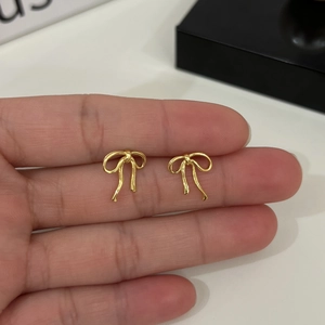 Macro view of dainty golden ribbon bow stud earrings held by hand for scale