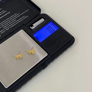 Macro view of gold bow earrings on a digital scale showing a weight of 1.07g