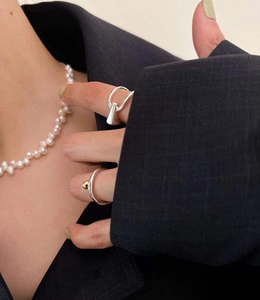 Gros plan sur des bagues en argent 925 et collier de perles sur un blazer noir chic