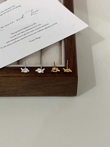 Macro detail of minimalist gold and silver knot stud earrings in a wooden jewelry box