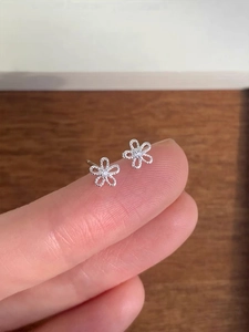 Macro detail of petite 925 sterling silver daisy stud earrings with zircon on a fingertip