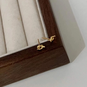 Close-up of golden minimalist knot stud earrings on a beige velvet jewelry display