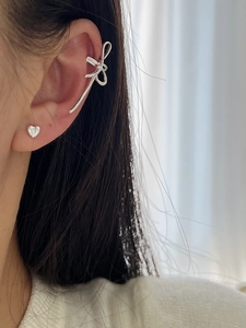 Gros plan d'un ear cuff nœud argenté et d'un clou d'oreille cœur sur l'oreille