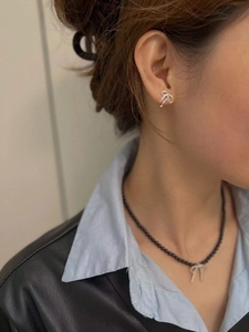 Detail view of silver bow earrings and black beaded necklace on a model