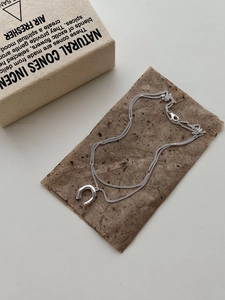 Detail of silver horseshoe pendant necklace with minimalist chain on natural paper background