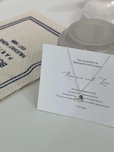 Detailaufnahme einer zarten silbernen Herz-Halskette auf einer minimalistischen Karte