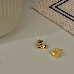 Dettaglio di orecchini a cuore dorati con trama ondulata e finitura lucida a specchio