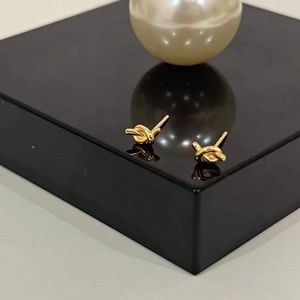 Detailed view of minimalist gold knot stud earrings on a sleek black display stand