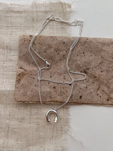 Detailed close-up of a polished silver horseshoe pendant necklace on textured fabric