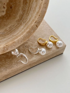 Detailed view of elegant C-shaped pearl earrings in gold and silver finish on stone