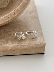 Close-up of silver bow earrings with round pearls on a textured stone display stand