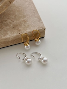 Detailed view of elegant gold and silver C-shaped pearl hook earrings on natural stone