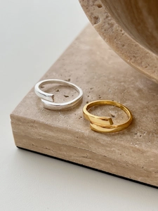 Detailed view of minimalist gold and silver open crossover rings on stone background