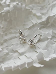Detailed close-up of 925 silver bow earrings with round white pearls on white background