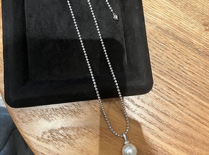 Detail of white pearl pendant on silver bead chain with heart tag on black velvet