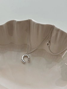 Polished silver horseshoe pendant necklace on a cream textured plate with lobster clasp