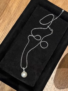 Detail view of large round white pearl pendant with diamond-encrusted clasp on silver chain