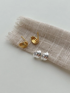 Détail des boucles d'oreilles croisées dorées et argentées sur un tissu en lin beige