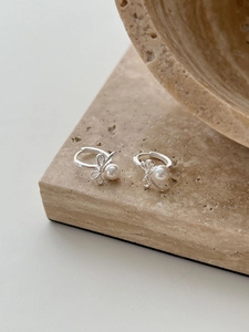 Close-up of silver bow earrings with round white pearls on a minimalist stone base