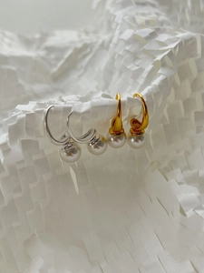 Detail view of gold and silver C-shaped pearl earrings on a white artistic paper stand