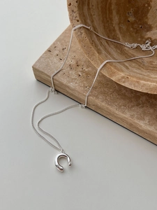 Minimalist silver U-shaped pendant necklace displayed on a textured stone prop