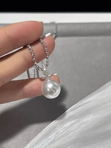Detailed view of large white pearl pendant with sparkling silver lobster clasp on a ball chain